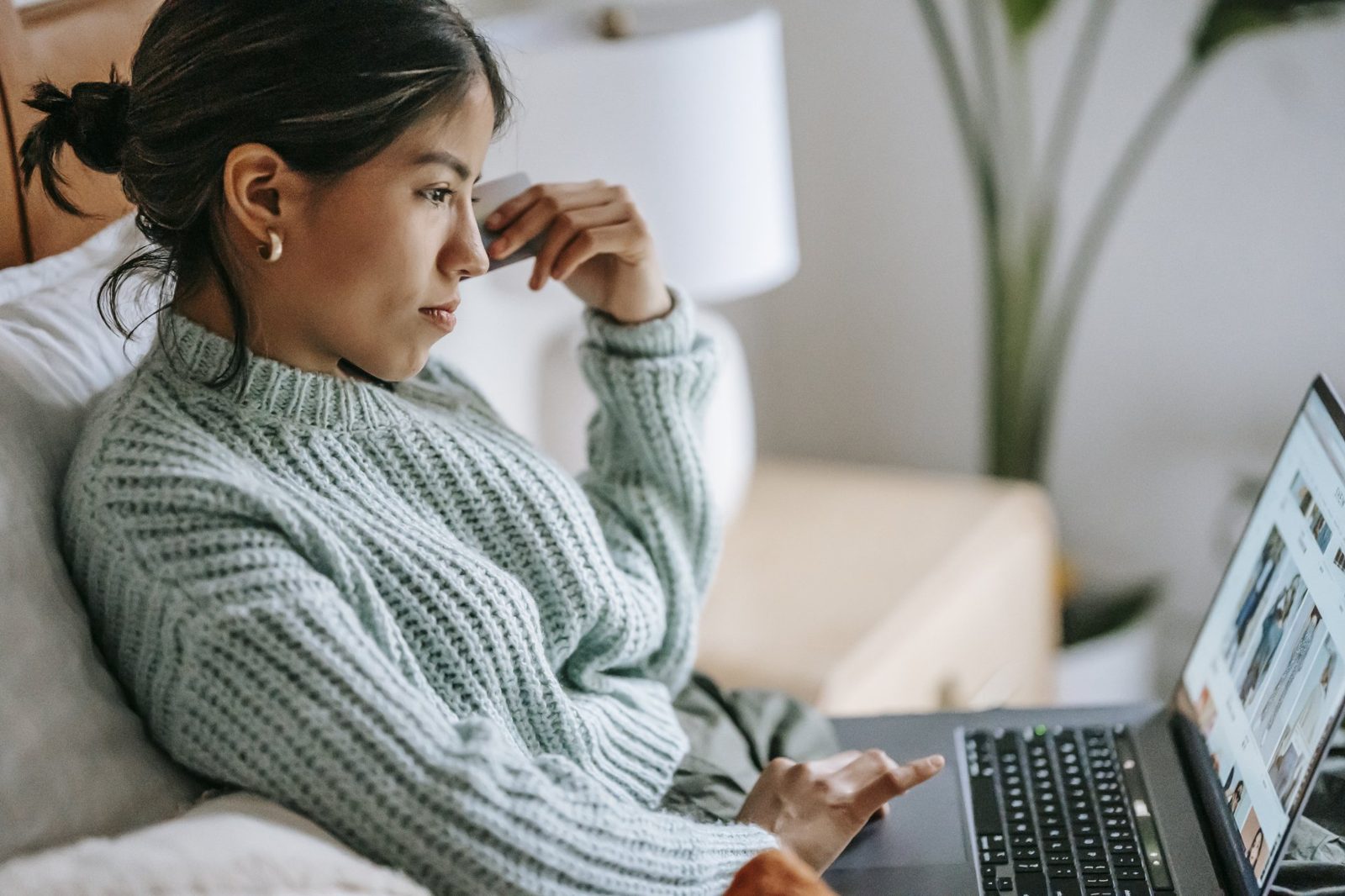 A woman is sitting on a couch using a laptop computer.