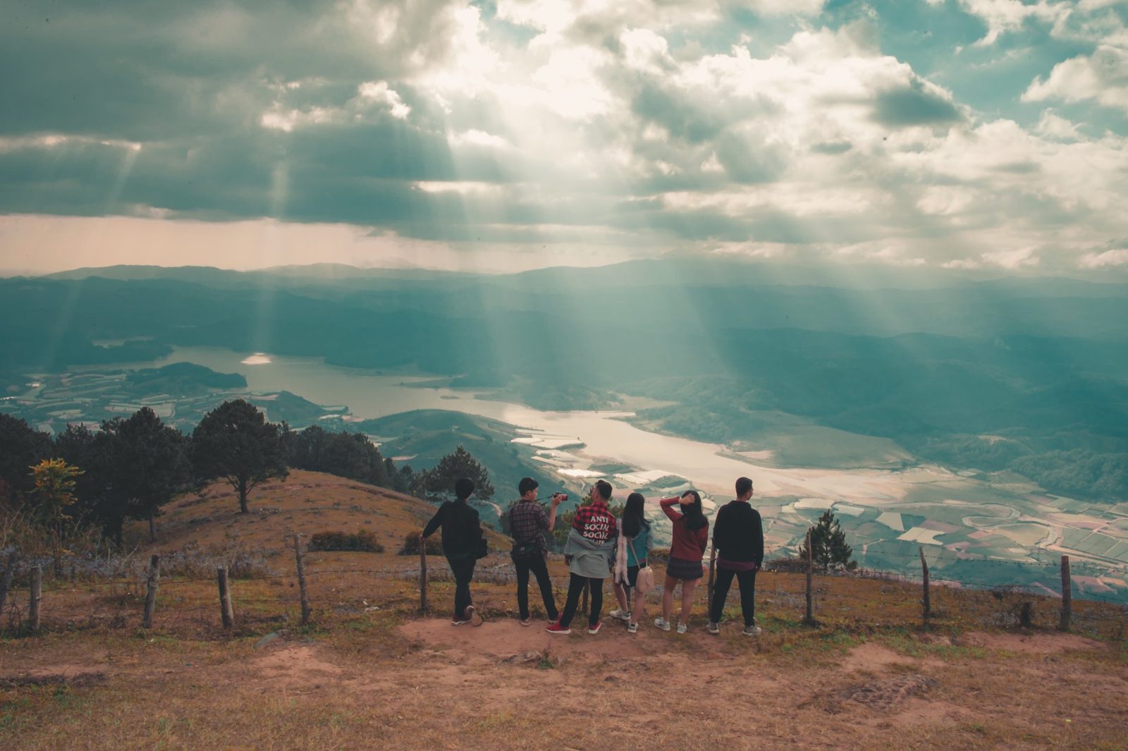 A group of people are standing on top of a hill overlooking a lake.